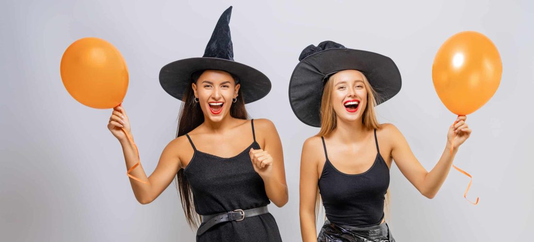 Happy Halloween! Two young women in black witch costumes on party on white background.
